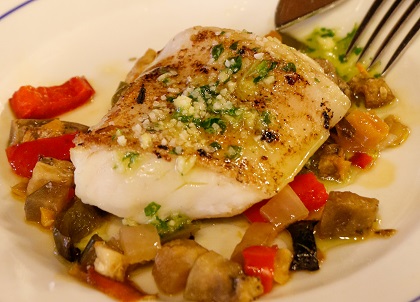 Pescado cocinado sobre verduras, con ajo y perejil